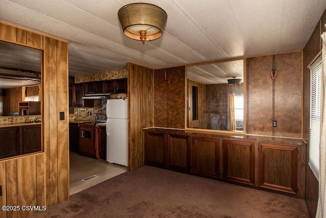 kitchen featuring white refrigerator, wooden walls, range, and light carpet