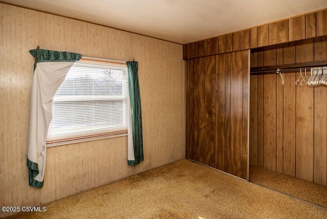 unfurnished bedroom featuring carpet floors, a closet, and wooden walls