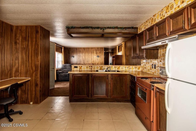 kitchen featuring wood walls, backsplash, white refrigerator, range, and kitchen peninsula