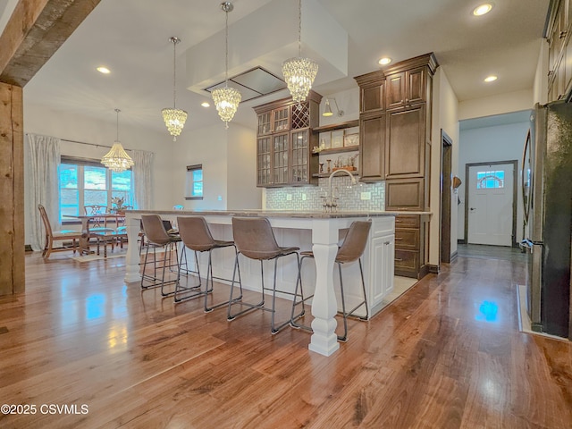 kitchen featuring a breakfast bar, tasteful backsplash, hanging light fixtures, stainless steel refrigerator, and hardwood / wood-style floors