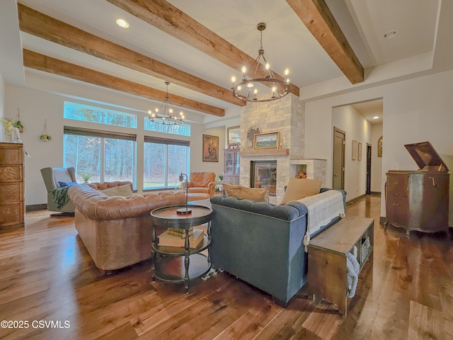 living room featuring beamed ceiling, a stone fireplace, dark wood-type flooring, and an inviting chandelier