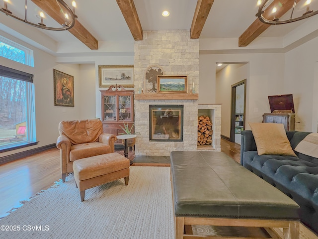 living room featuring beam ceiling, a notable chandelier, a stone fireplace, and light hardwood / wood-style flooring