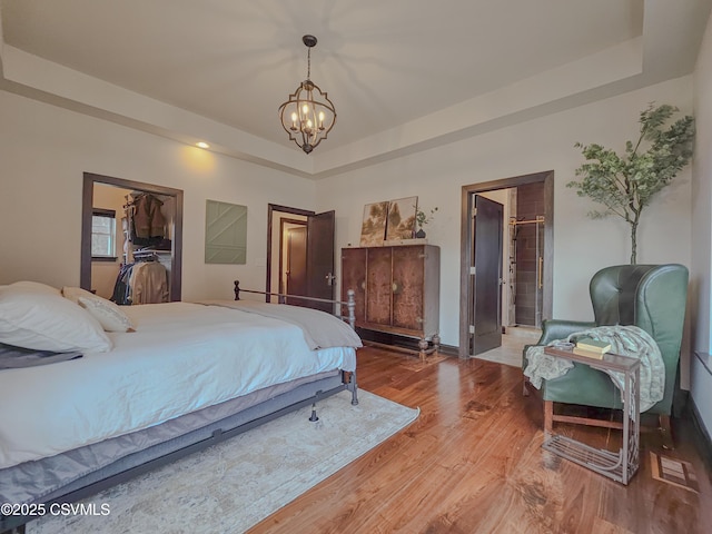 bedroom with hardwood / wood-style floors, a notable chandelier, and a raised ceiling