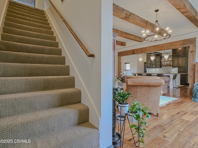 stairs featuring a notable chandelier, beam ceiling, and wood-type flooring