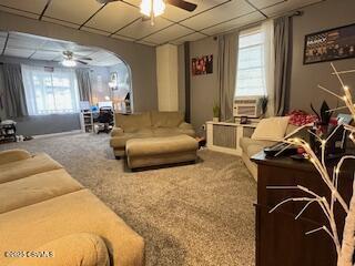 carpeted living room with a drop ceiling, cooling unit, and ceiling fan