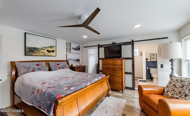 bedroom with ensuite bathroom, a barn door, ceiling fan, and light wood-type flooring