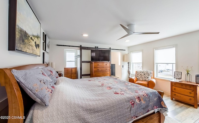 bedroom featuring multiple windows, a barn door, ceiling fan, and light wood-type flooring