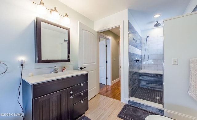 bathroom with hardwood / wood-style flooring, vanity, and a tile shower