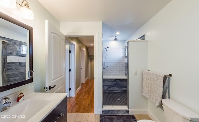 bathroom featuring hardwood / wood-style flooring, tiled shower, vanity, and toilet