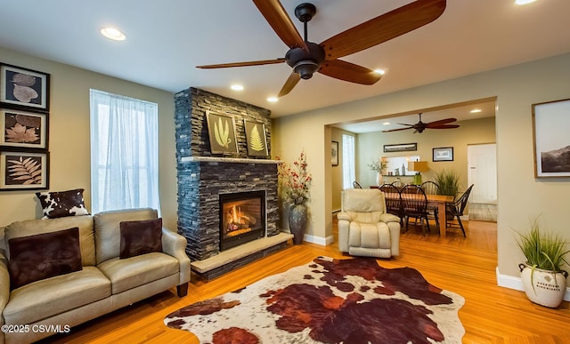 living room featuring ceiling fan, a fireplace, and light hardwood / wood-style floors