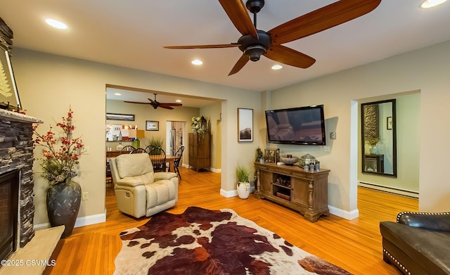 living room with ceiling fan, a stone fireplace, light hardwood / wood-style floors, and a baseboard heating unit