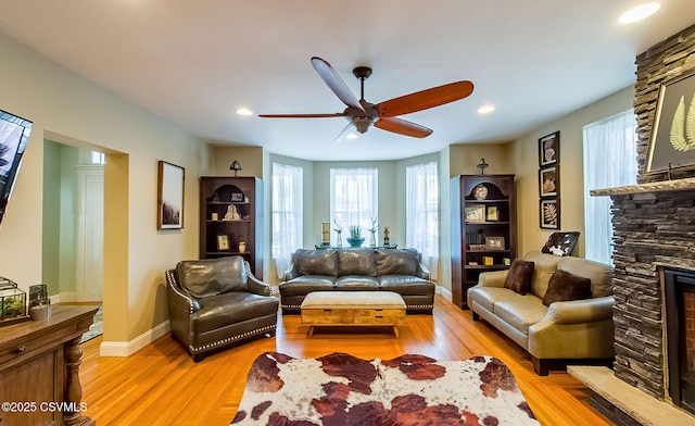 living room featuring ceiling fan, a fireplace, and light wood-type flooring