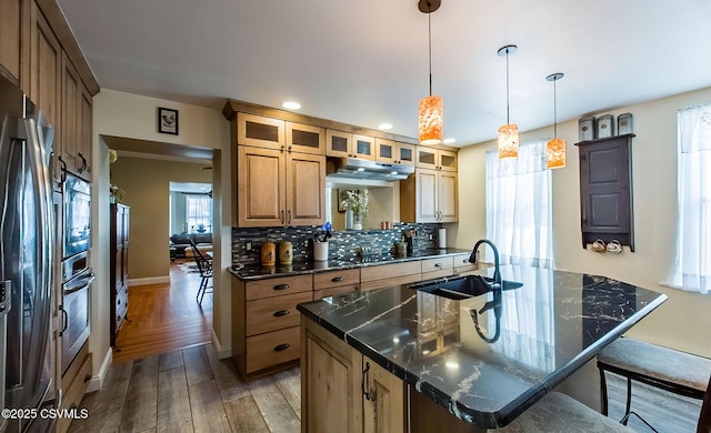 kitchen with pendant lighting, sink, backsplash, a center island with sink, and light hardwood / wood-style flooring