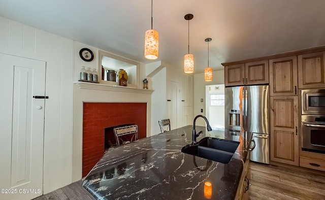 kitchen with pendant lighting, sink, stainless steel appliances, dark stone counters, and light wood-type flooring