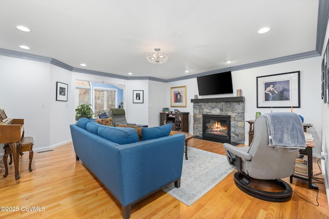 living room featuring ornamental molding, a stone fireplace, and light hardwood / wood-style floors