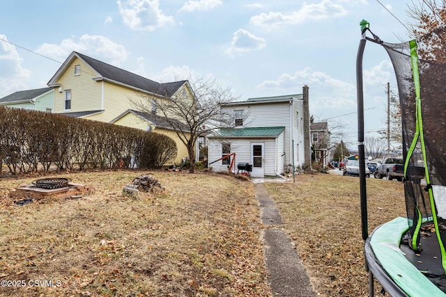 rear view of property with a trampoline and an outdoor fire pit