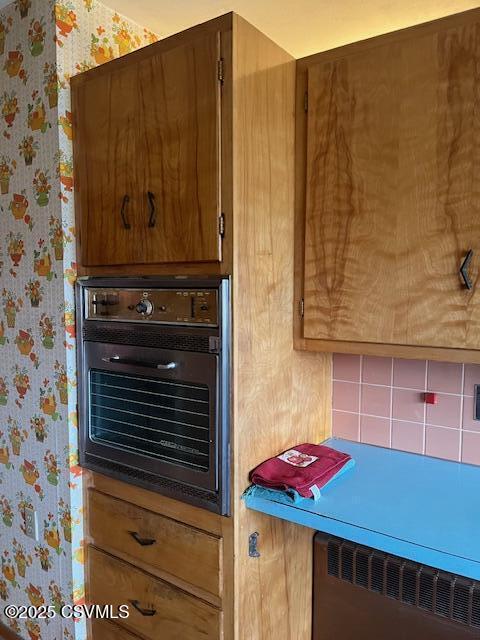interior details with wall oven, wallpapered walls, brown cabinetry, and radiator