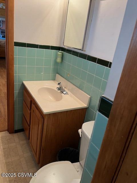 half bath featuring wainscoting, toilet, vanity, and tile walls