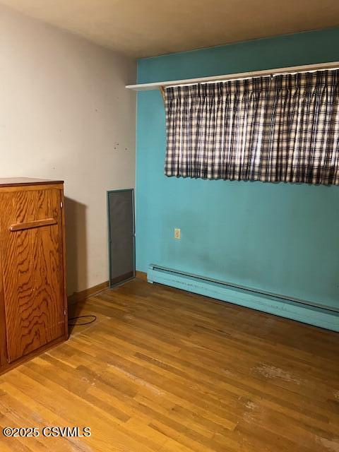 spare room featuring wood finished floors and a baseboard heating unit