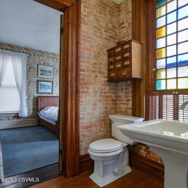 bathroom featuring brick wall, hardwood / wood-style floors, and toilet