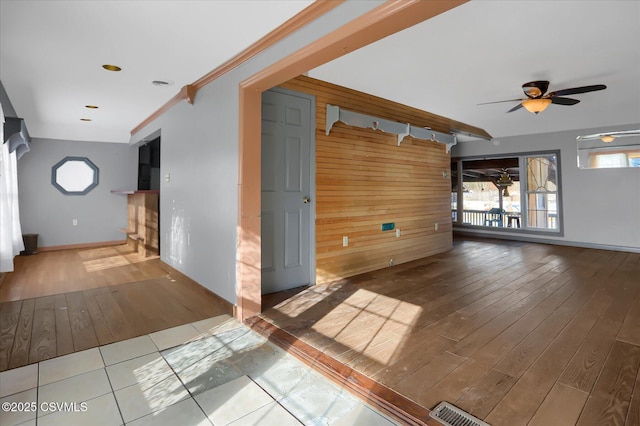 empty room with ceiling fan, ornamental molding, light wood-type flooring, and wood walls