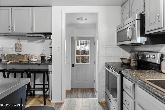 kitchen featuring white cabinetry, dark stone countertops, stainless steel appliances, tasteful backsplash, and light wood-type flooring