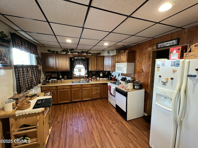 kitchen featuring sink, a paneled ceiling, wooden walls, dark hardwood / wood-style flooring, and white appliances