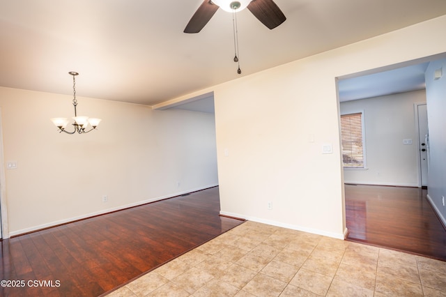 spare room with ceiling fan with notable chandelier, wood finished floors, and baseboards