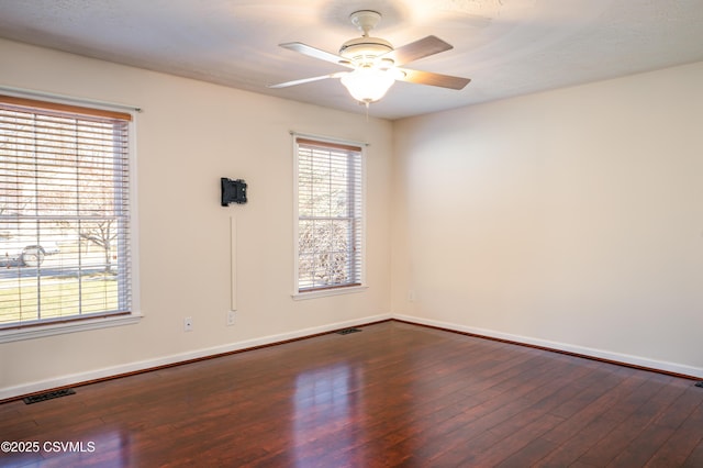 empty room with ceiling fan, visible vents, baseboards, and dark wood finished floors