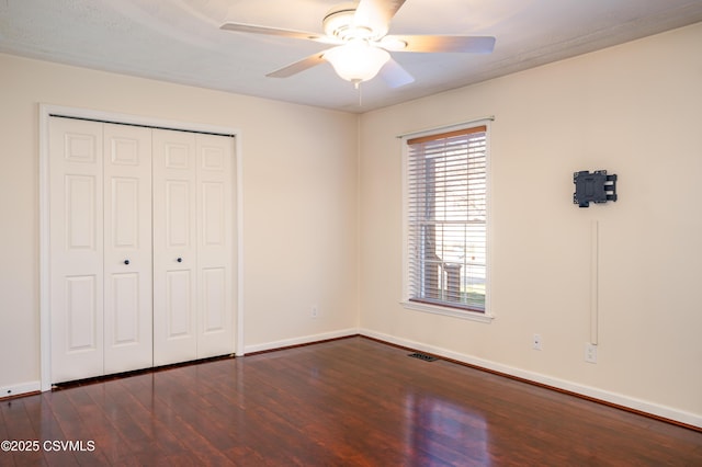 unfurnished bedroom with a ceiling fan, visible vents, baseboards, dark wood-style flooring, and a closet