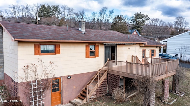 back of house featuring stairs, a deck, a chimney, and a shingled roof