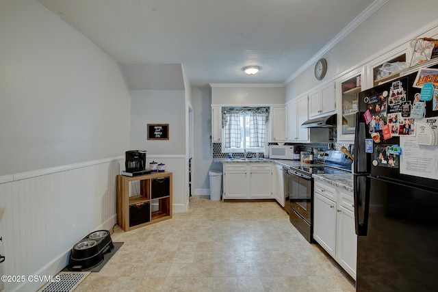 kitchen featuring a wainscoted wall, white cabinets, a sink, under cabinet range hood, and black appliances