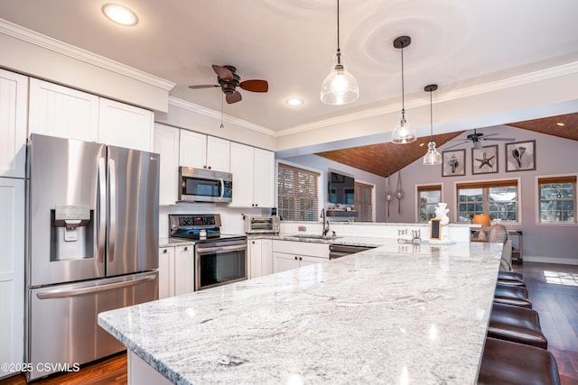 kitchen featuring white cabinets, appliances with stainless steel finishes, a breakfast bar, pendant lighting, and a sink