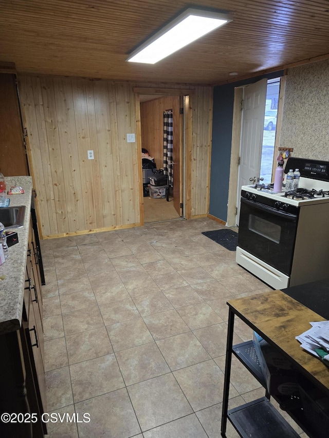 kitchen featuring light tile patterned floors, gas range, wooden walls, and wooden ceiling