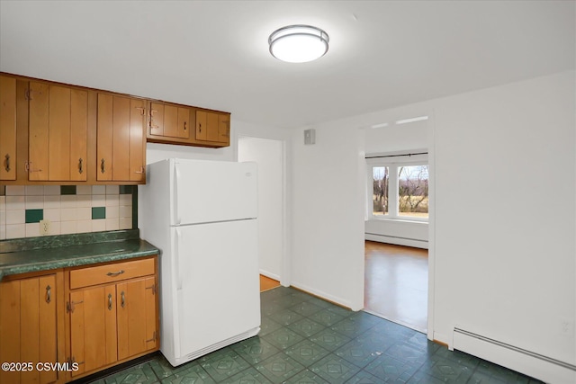 kitchen featuring baseboard heating, dark countertops, backsplash, and freestanding refrigerator