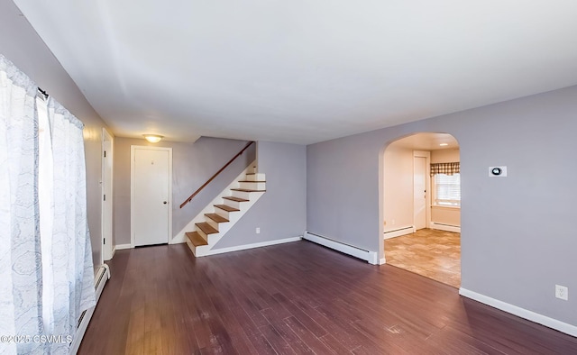 unfurnished room with a baseboard heating unit, arched walkways, stairway, and wood finished floors