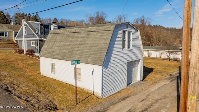 exterior space featuring a garage, a shingled roof, dirt driveway, a gambrel roof, and a yard