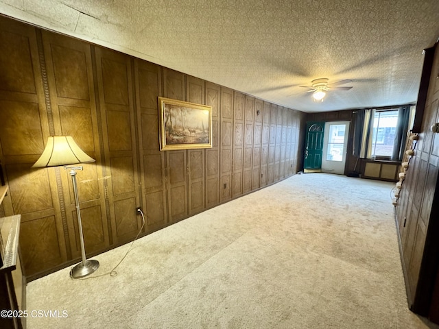 carpeted spare room featuring ceiling fan, a textured ceiling, and wood walls