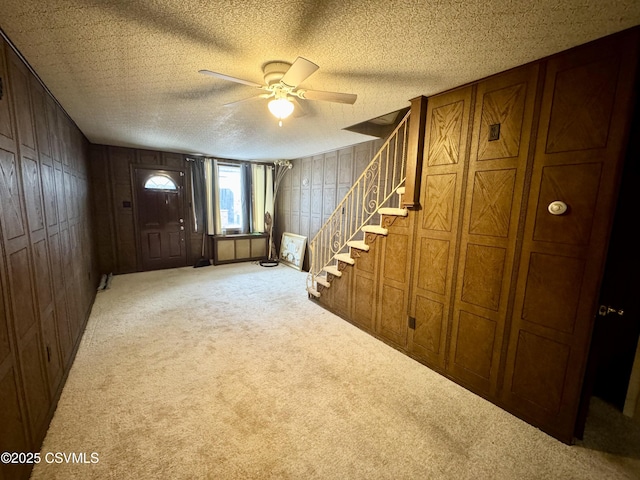 foyer with ceiling fan, carpet floors, a textured ceiling, and wood walls