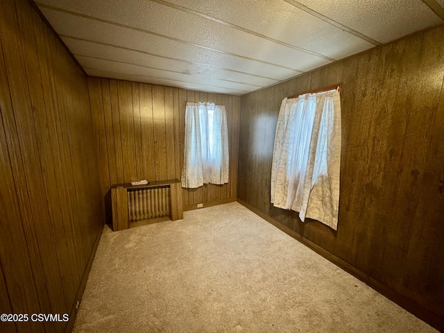 carpeted empty room with radiator heating unit and wooden walls