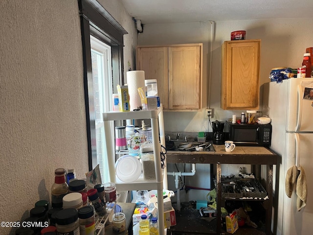 kitchen featuring black microwave, light brown cabinetry, and freestanding refrigerator