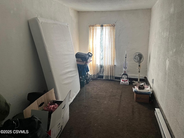 misc room featuring a baseboard heating unit, dark carpet, a textured ceiling, and a textured wall