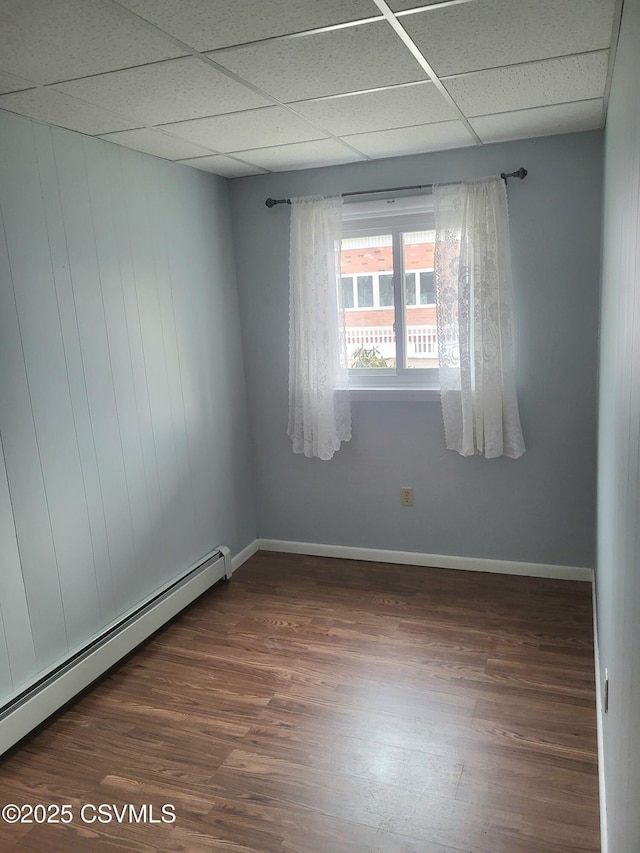 unfurnished room featuring a baseboard radiator, dark wood-style flooring, a drop ceiling, and baseboards