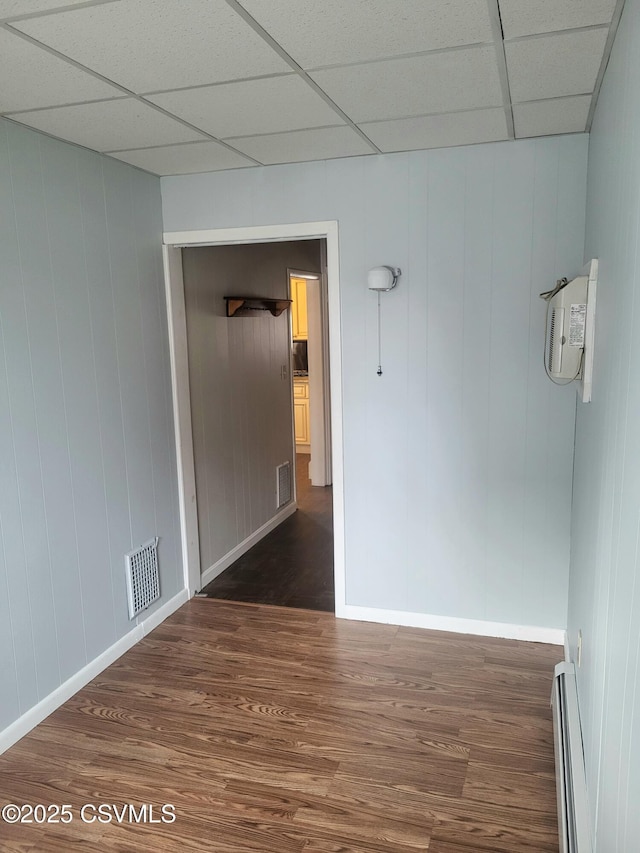 unfurnished room featuring a paneled ceiling, a baseboard heating unit, visible vents, and dark wood finished floors