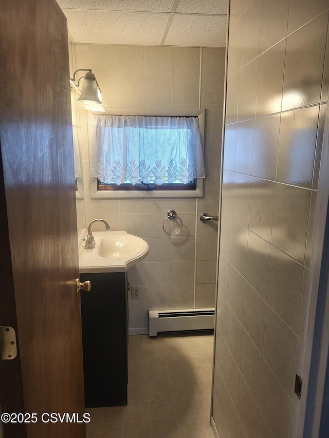 bathroom with tile walls, a paneled ceiling, vanity, and baseboard heating