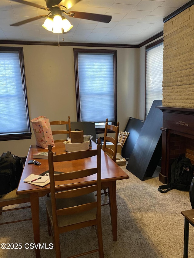 carpeted dining room featuring ceiling fan, a fireplace, and crown molding