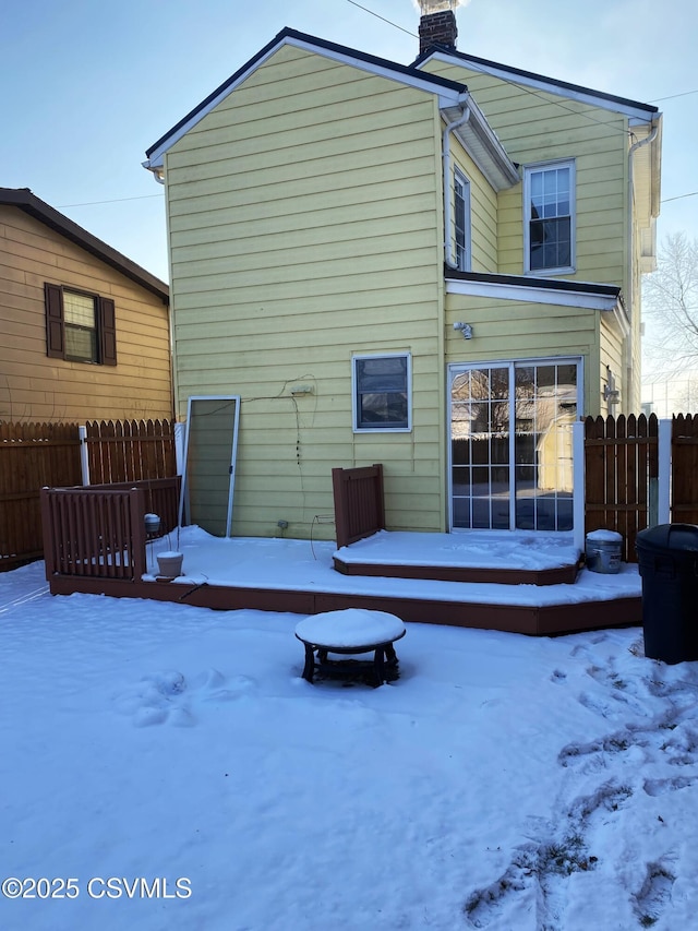 snow covered back of property with an outdoor fire pit, a chimney, and fence