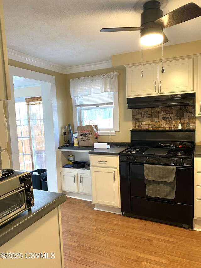 kitchen featuring light wood finished floors, black range with gas cooktop, dark countertops, under cabinet range hood, and white cabinetry