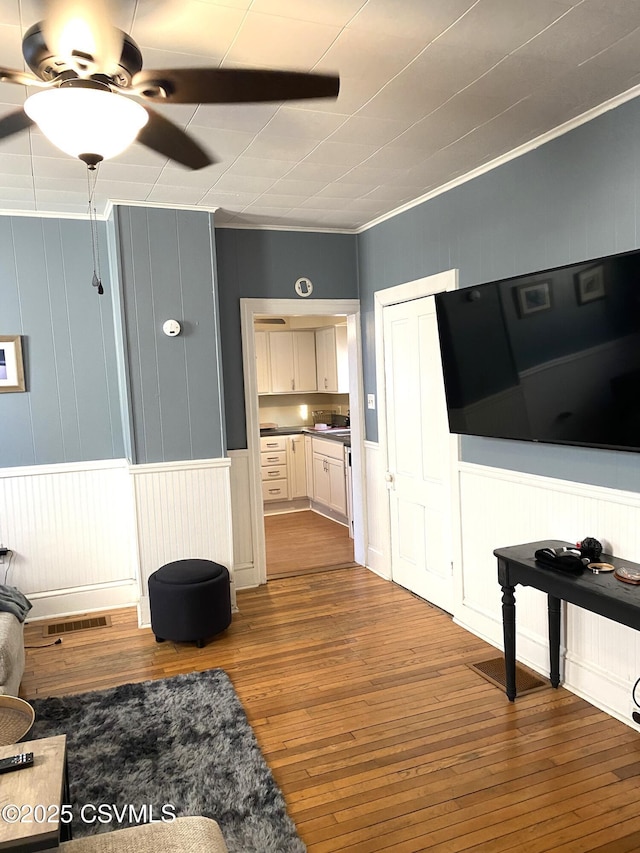 living area with ceiling fan, ornamental molding, wood-type flooring, and visible vents