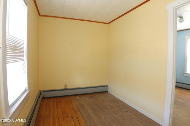 empty room with ornamental molding, wood-type flooring, and a baseboard heating unit